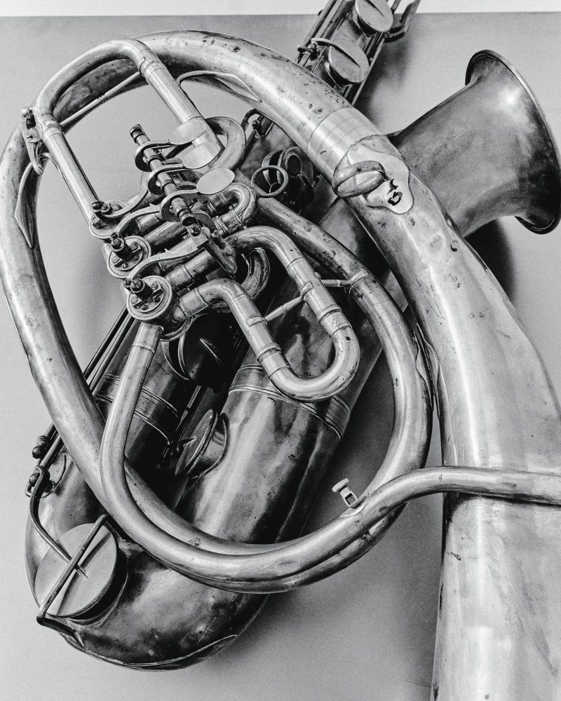 Monochrome shot of a saxophone and a euphonium intertwining, creating an abstract pattern with their metallic curves and keys.