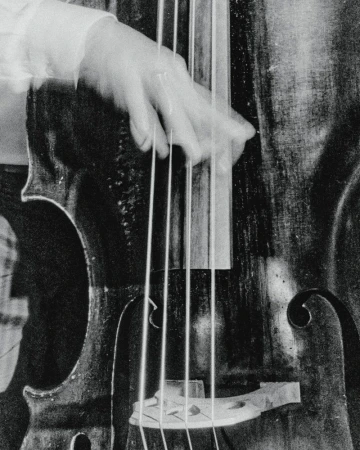A close-up black and white image shows a person playing an upright bass. The person's hand is blurred, creating a sense of motion.