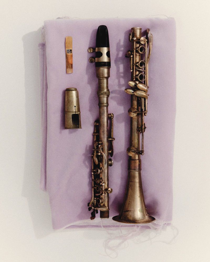 Still life photograph featuring two clarinets and clarinet parts laid out on a light purple cloth surface against a bright background.