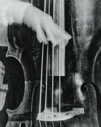Monochrome close-up of a musician's hand captured in motion playing the strings of an upright double bass.