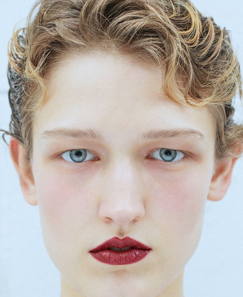 Close-up portrait of model Pauline Schubach with dark red lipstick and wet blonde hair against a plain white background