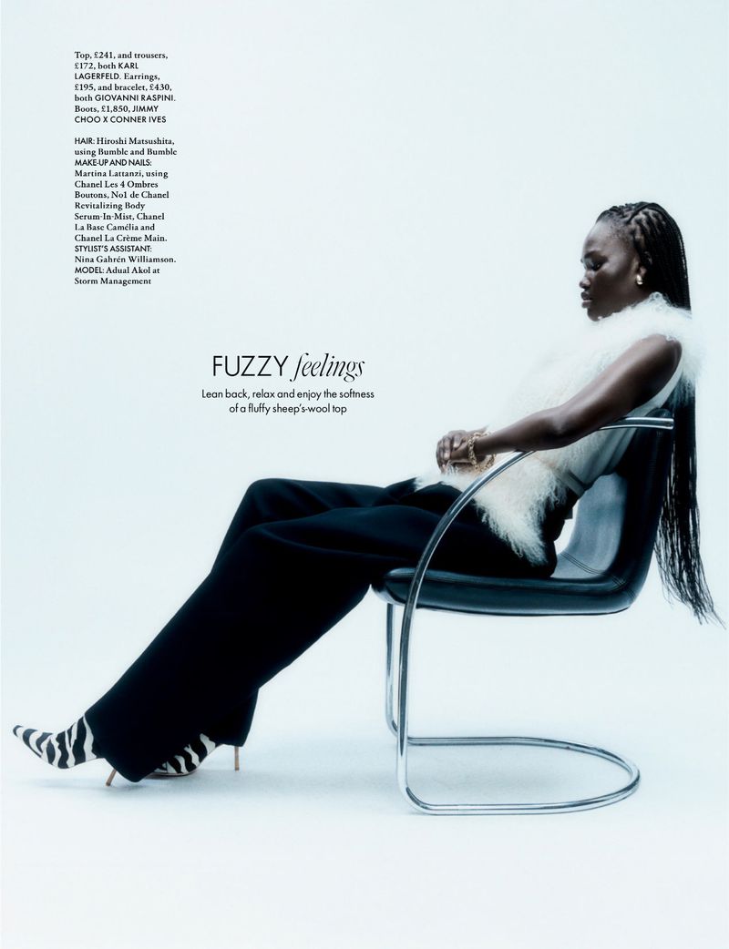 Fashion editorial shot of an African-American woman in a white top and black pants sitting in a modern chair against a white backdrop.