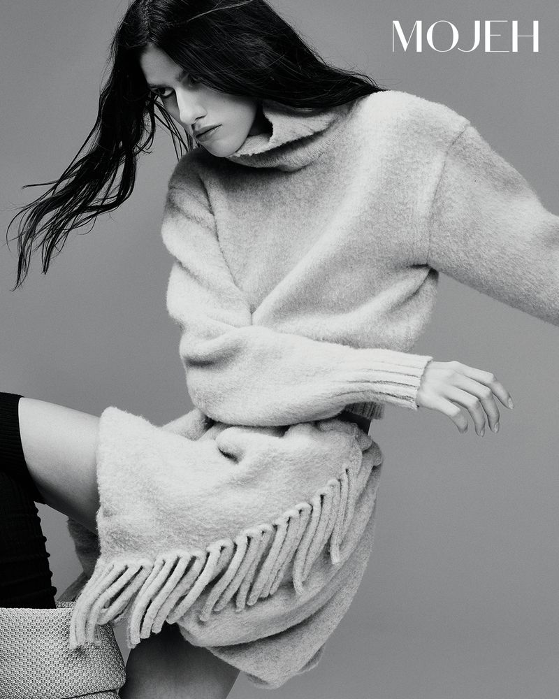 Model in a grey fringed turtleneck dress against a plain grey studio background for Mojeh Magazine editorial.