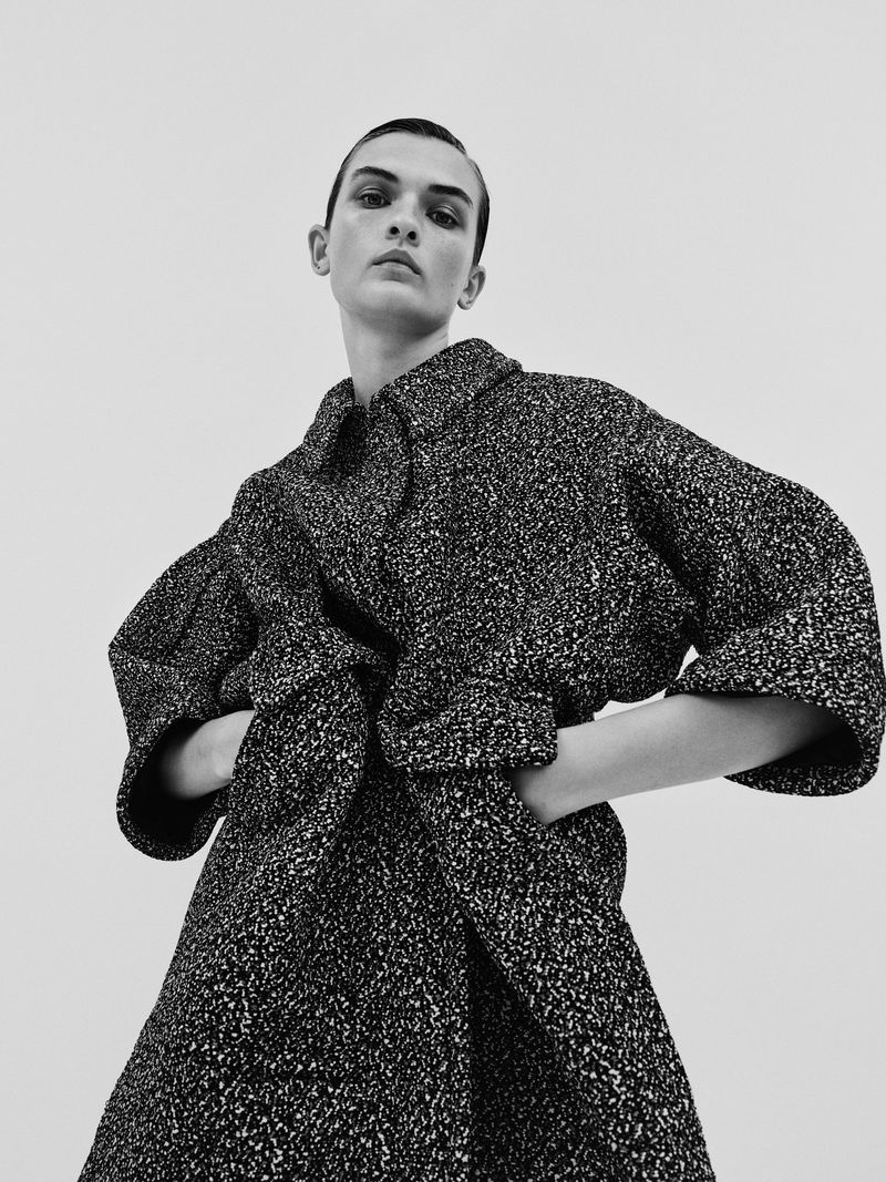 Fashion shot featuring a single female model with short hair in a stylish, speckled wool coat with her hands tucked into the pockets.