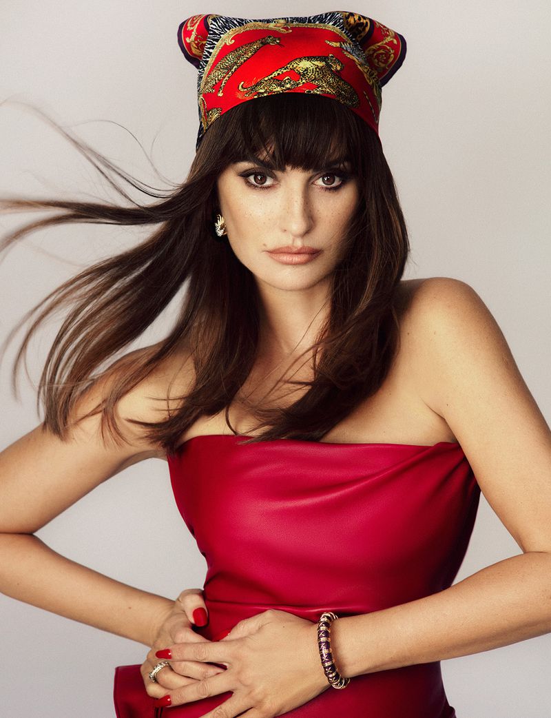 Penelope Cruz wearing a red strapless top and printed headscarf against a white background