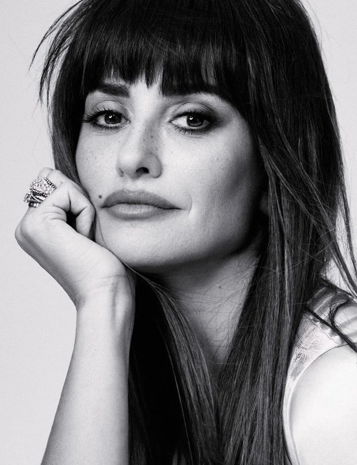 Black and white portrait of actor Penélope Cruz resting her chin on her hand with rings.