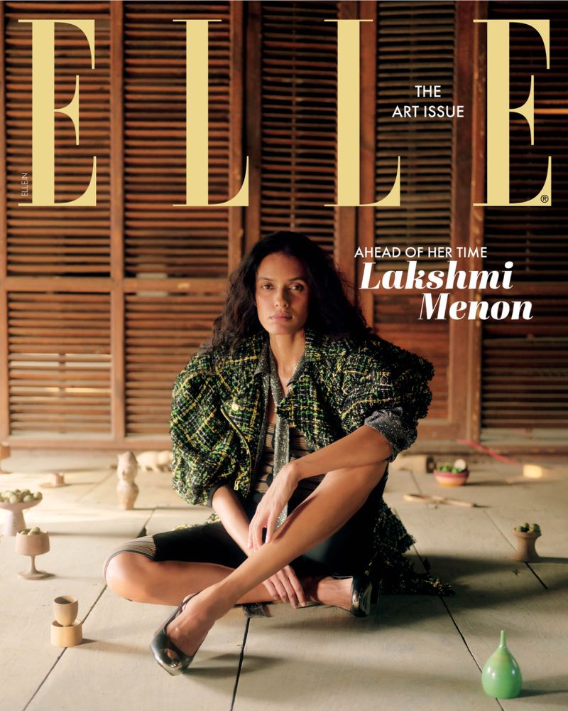 Magazine cover featuring Lakshmi Menon, seated in an indoor setting, wearing a textured green jacket and dark skirt, with curated objects.