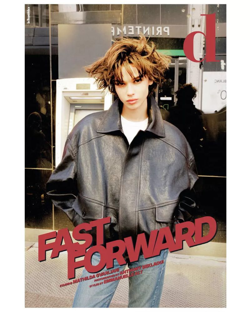 Fashion magazine cover featuring a young adult with a messy bob haircut, wearing a black leather jacket, standing outdoors.