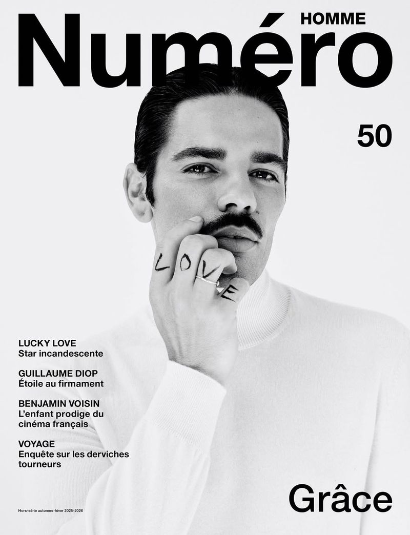 Black and white magazine cover featuring a portrait of a man with a mustache, wearing a white turtleneck, and hand tattoos.