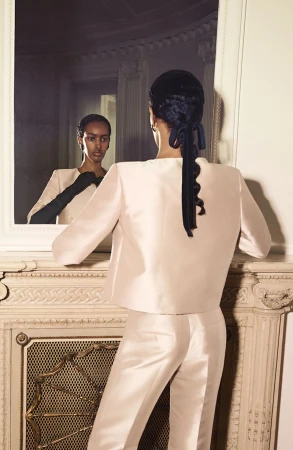 Model seen from behind facing a mirror, wearing a pale satin two-piece suit and dark gloves, styled for Alberta Ferretti resort 25.