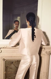 Model seen from behind facing a mirror, wearing a pale satin two-piece suit and dark gloves, styled for Alberta Ferretti resort 25.