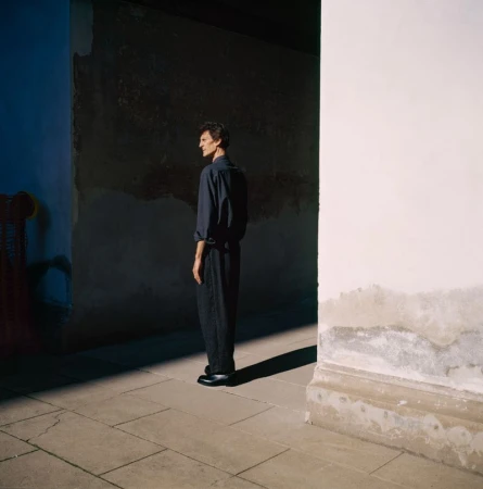 Nicolas Duée standing in profile wearing a dark navy shirt and pleated trousers in dramatic architectural sunlight for Toast.