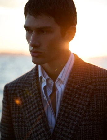 Luka Tesic wearing a houndstooth blazer and striped shirt outdoors at sunset.