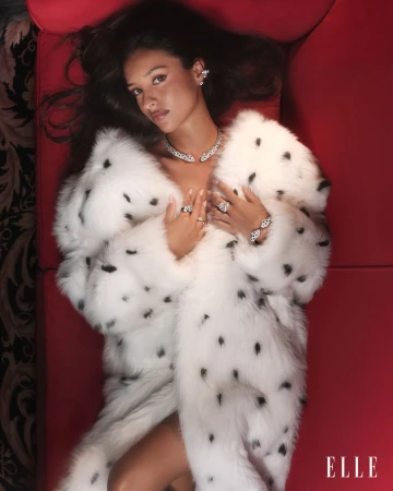 Elegant woman in a spotted fur coat reclines on a red surface, adorned with jewelry, and captured in a glamour shot. Fashion photography.