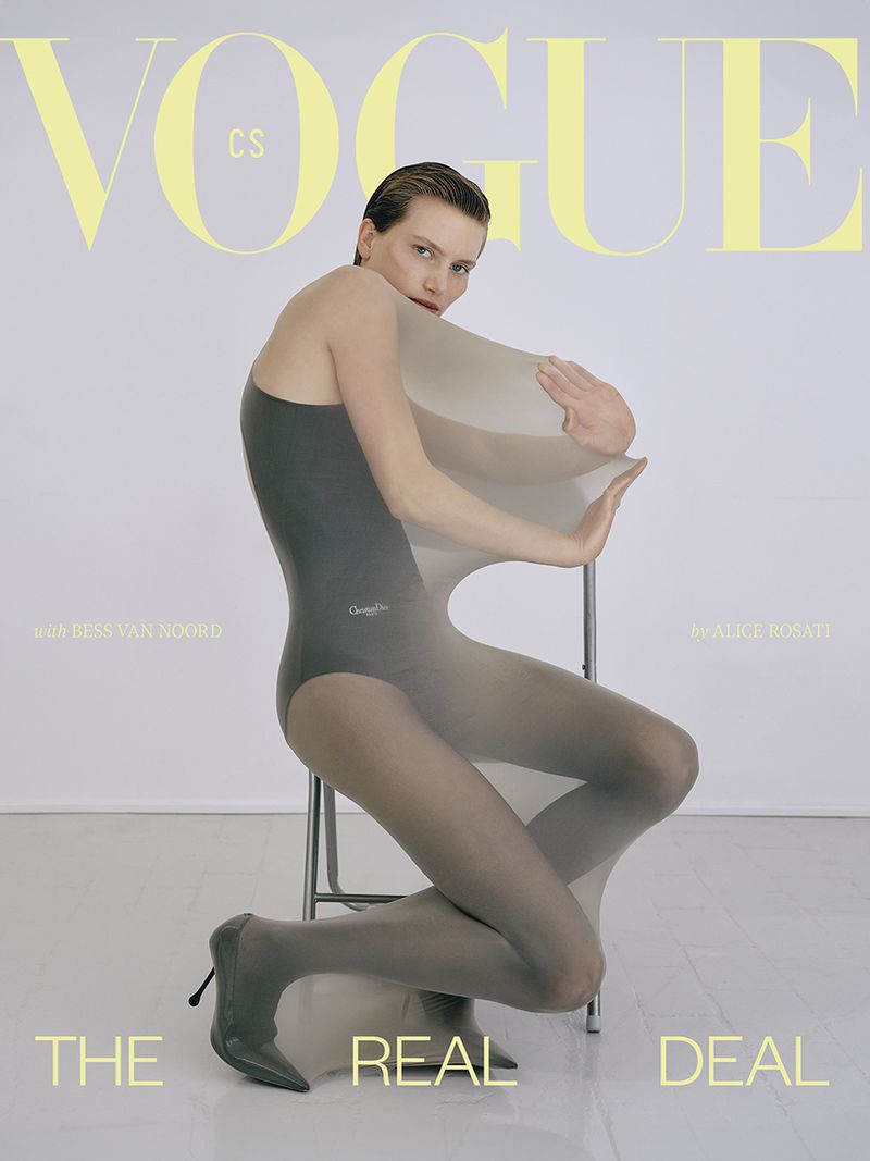 Vogue cover featuring a woman in a bodysuit and sheer tights kneeling next to a chair in a photo studio against a white backdrop.