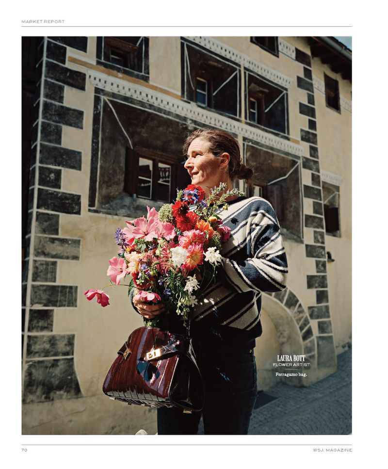 Woman in striped sweater and holding a colorful flower bouquet and dark purse outside a stucco building. Editorial fashion shot.