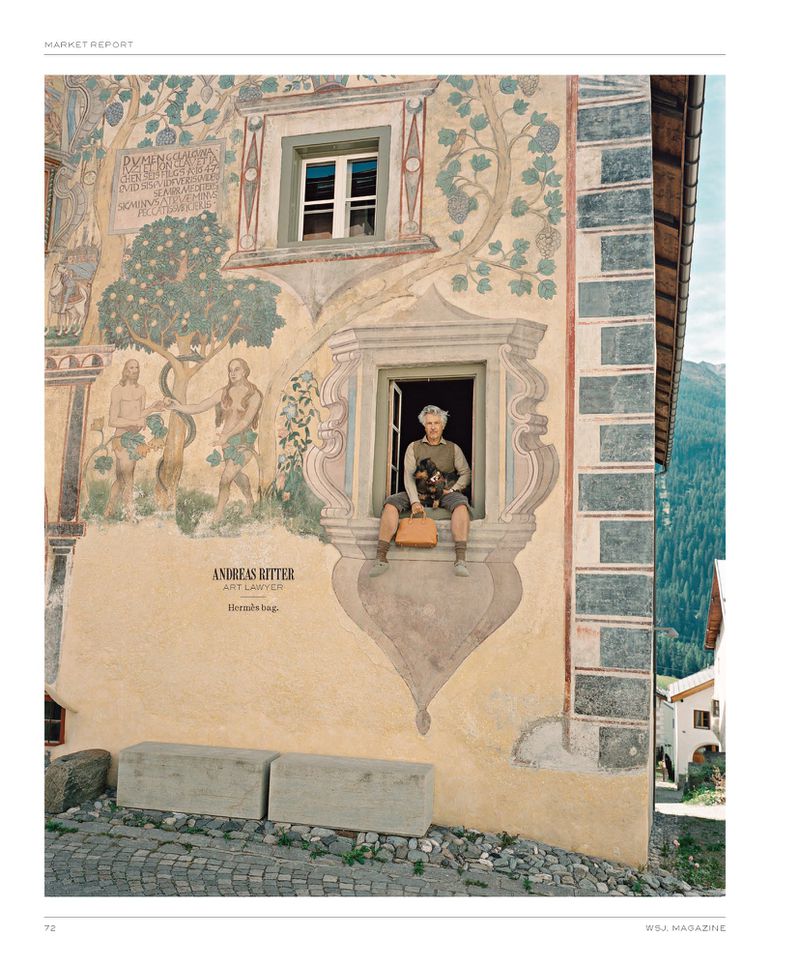 Person sits in a window of a building with a painted facade and tree, holding a stuffed animal and tan bag, with mountain backdrop.