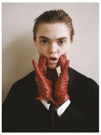 Close-up portrait of a young adult woman with wet-look hair, wearing red leather gloves that frame her face, and a dark blazer.