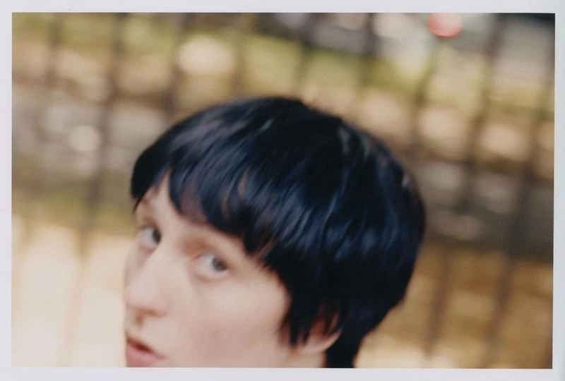 Close up portrait of a young adult female with short dark hair looking at the camera against an abstract neutral backdrop.