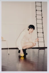 Model squatting while touching a yellow fruit in a room with a tall ladder prop, captured for Lula Japan editorial Step Aside.