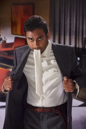Portrait of a man in a suit with a white cloth in his mouth, looking directly at the camera, in an indoor environment with gray walls.