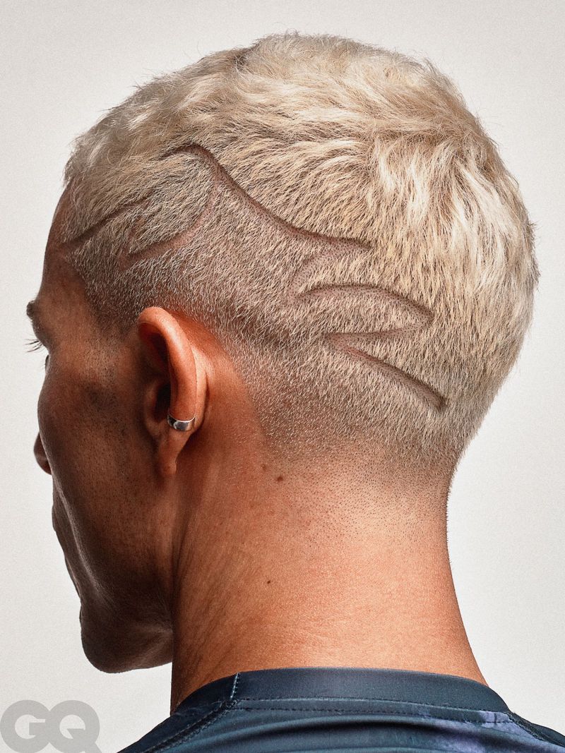 Close-up studio shot of a man with short blonde hair and a modern artistic hair design on the side of his head.