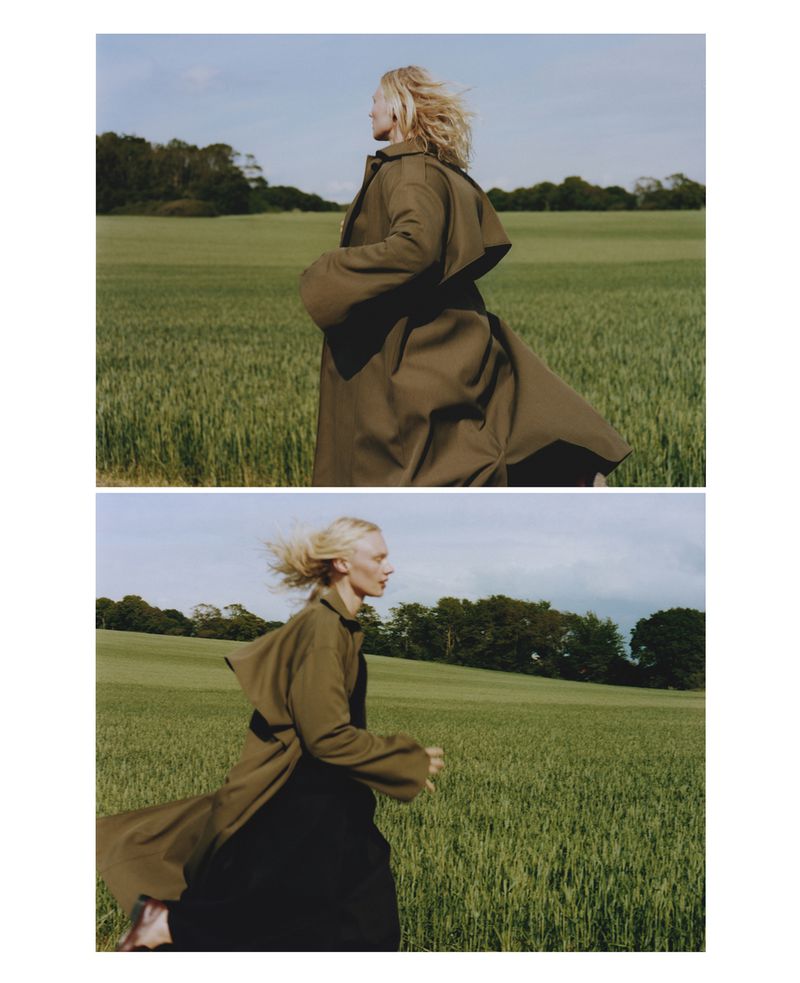 Woman in trench coat runs through wheat field on sunny day. Fashion editorial shot of blonde adult female in rural environment.