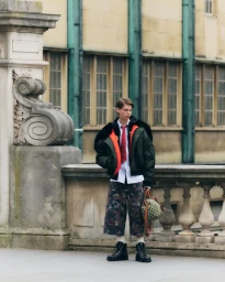 Model Ruben Long standing on a stone terrace wearing an oversized bomber jacket, red tie, patterned wide culottes, and black boots.