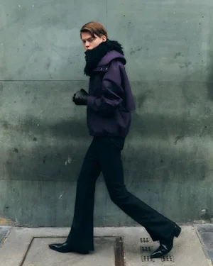 Model Ruben Long walking in a purple hooded jacket with black fur trim, black flared trousers, and pointed leather boots.