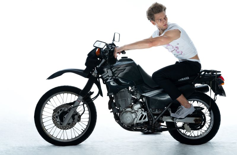 A fair-skinned adult male is sitting on a Yamaha motorcycle in a photo studio with bright white background, looking toward the right.