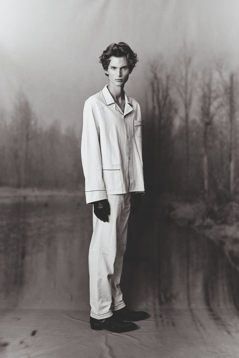 Young male model wearing light pajamas standing against a painted forest backdrop for a Numéro France editorial