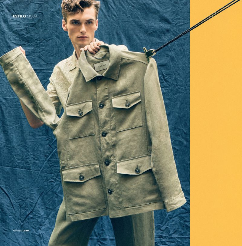 Male fashion model presents a light green button-down jacket; studio shot against blue and yellow backdrop with visible clothing rack.