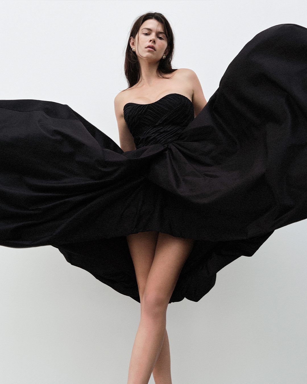 Model wearing a black strapless mini dress with a dramatic billowing skirt against a white backdrop.