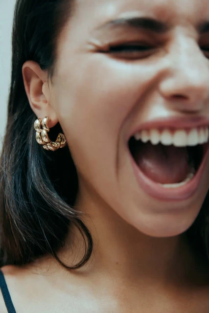 Close-up studio shot of a smiling woman with dark hair wearing gold hoop earrings, showcasing her happy expression and jewelry.