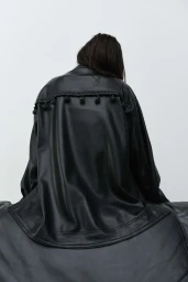 Model seen from behind wearing a black leather jacket with fringe detail against a plain white background