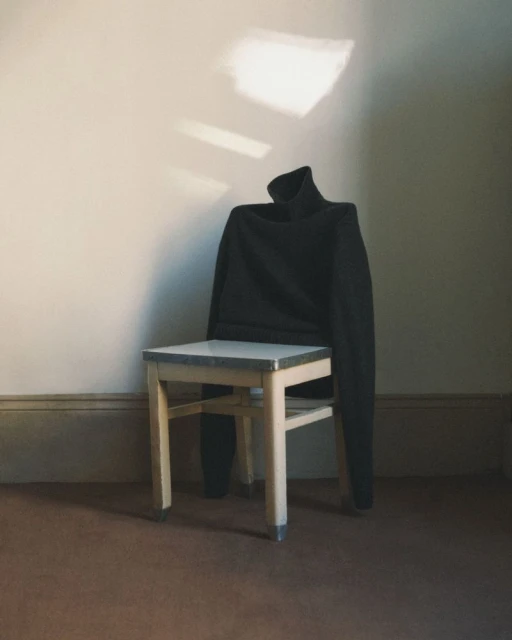 Black turtleneck sweater draped over a wooden chair in a room with natural light creating shadows on the wall.