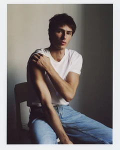 Clément Laguardia seated in a white t-shirt and light wash denim jeans against a muted neutral wall.