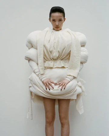 Model Xiao Wen Ju wearing avant-garde sculptural white knitwear against a plain studio background for HommeGirls.