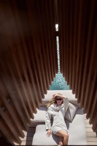 Chiara Ferragni reclining on a sun lounger in a white mini dress and sunglasses, framed through vertical wooden slats.