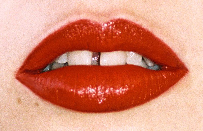 Close-up of bright red lipstick on full lips, revealing teeth with a gap. Focus on beauty and cosmetic application.