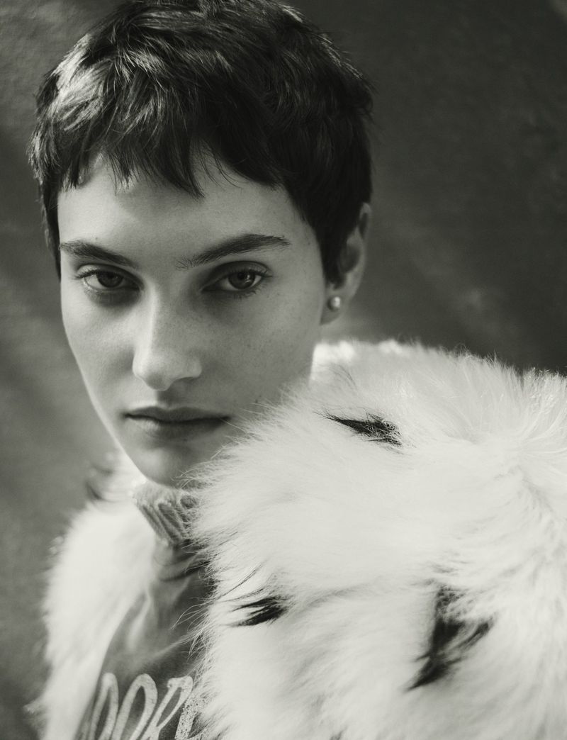 Black-and-white portrait of a young adult woman with short, dark hair wearing a sweater and a white fur stole, looking at the camera.