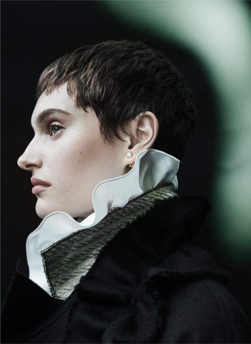 Profile portrait of an adult female with short brown hair wearing a black jacket and a white ruffle collar against a dark background.