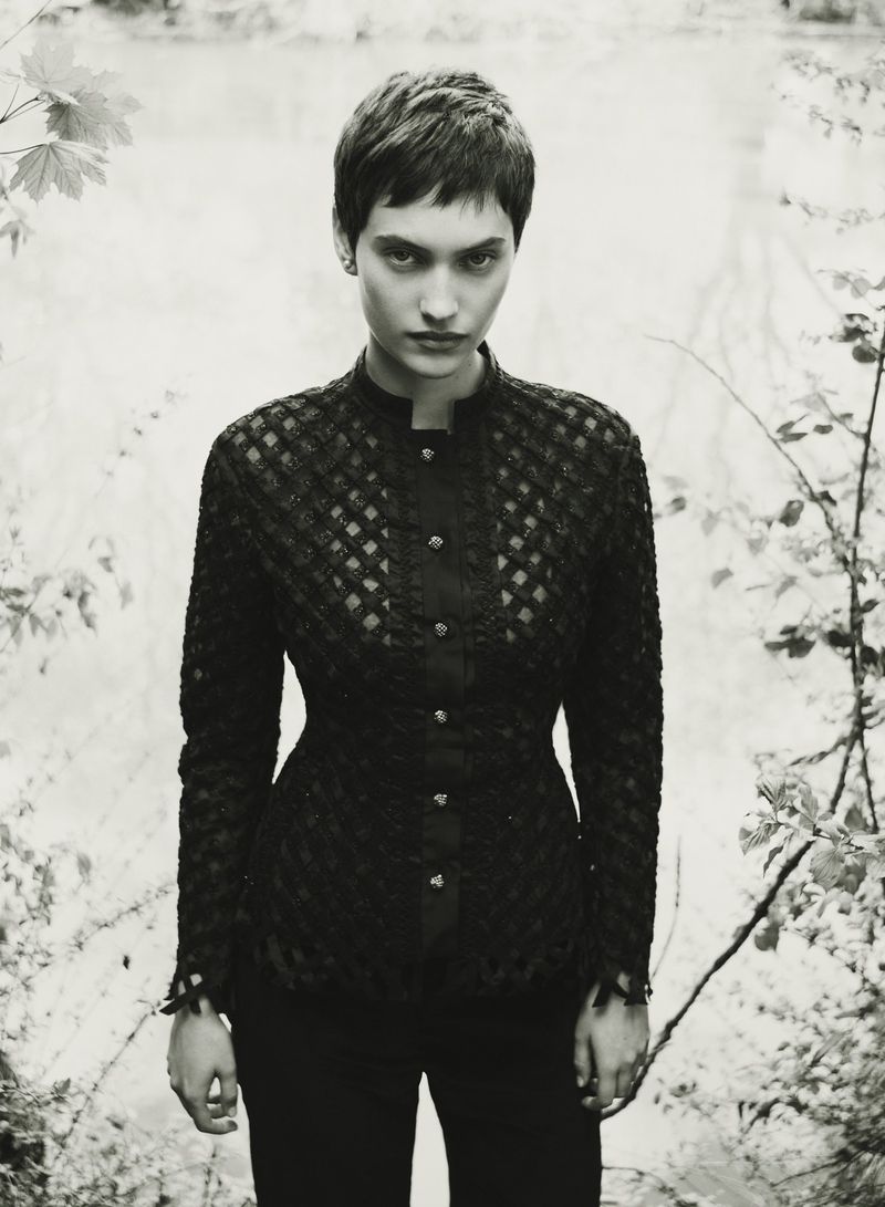 Monochrome portrait of a young adult female model with a short haircut wearing a black patterned jacket with a nature background.