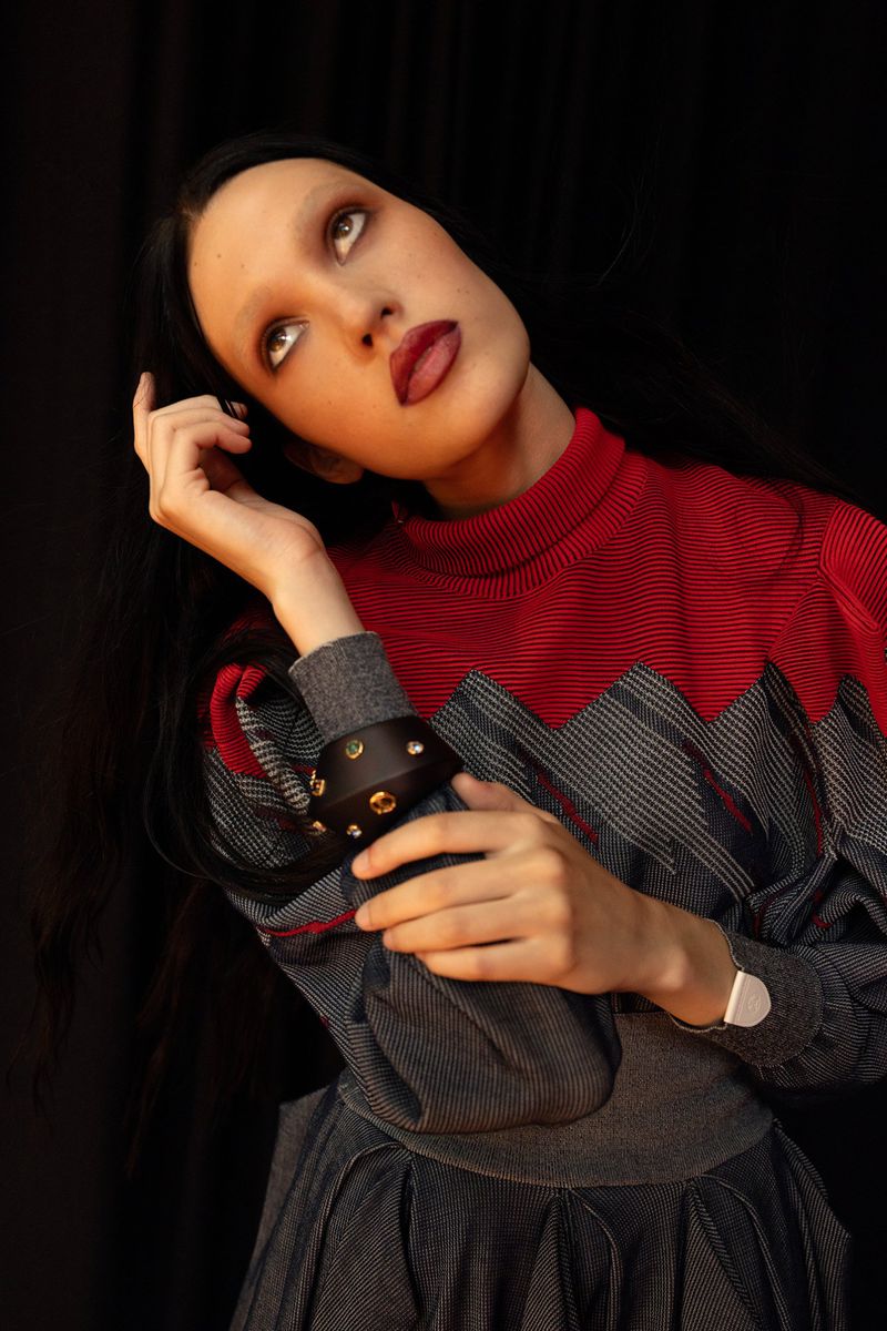 Adult female fashion model with dark hair and gray dress and red top posing in a studio with dark background looking up.