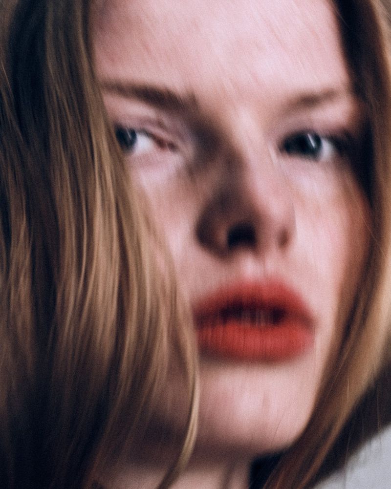Close-up portrait of model Elise Swain with soft motion blur, parted red lips, and brown hair framing her face.