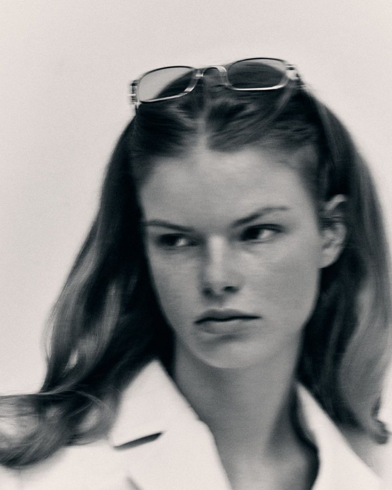 Portrait of a woman with glasses on her head in a studio. The image is monochromatic and features a neutral background.