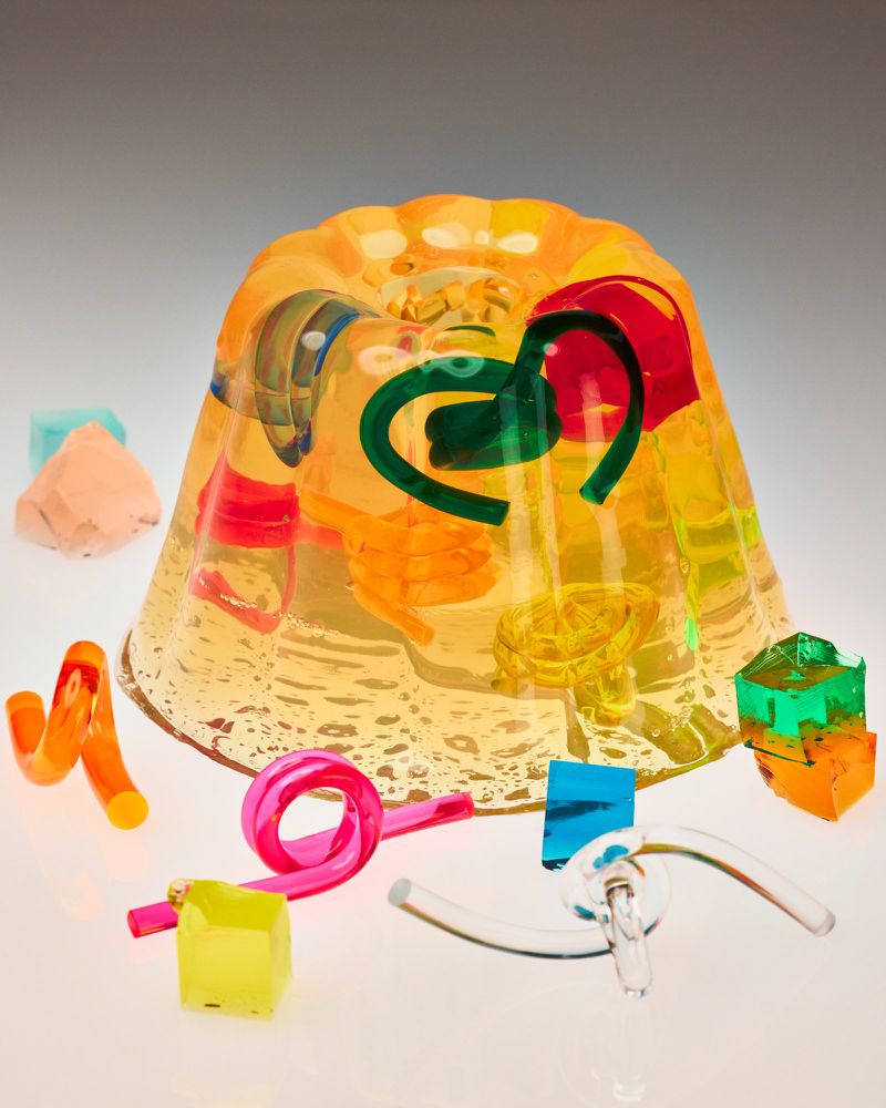 Vibrant yellow jelly mold filled with colorful gelatin shapes, set against a gradient background, with scattered gelatin cubes.