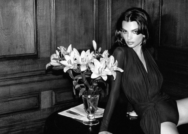 Monochrome portrait of a young woman in a dark dress with a flower arrangement on a table and paneled background.