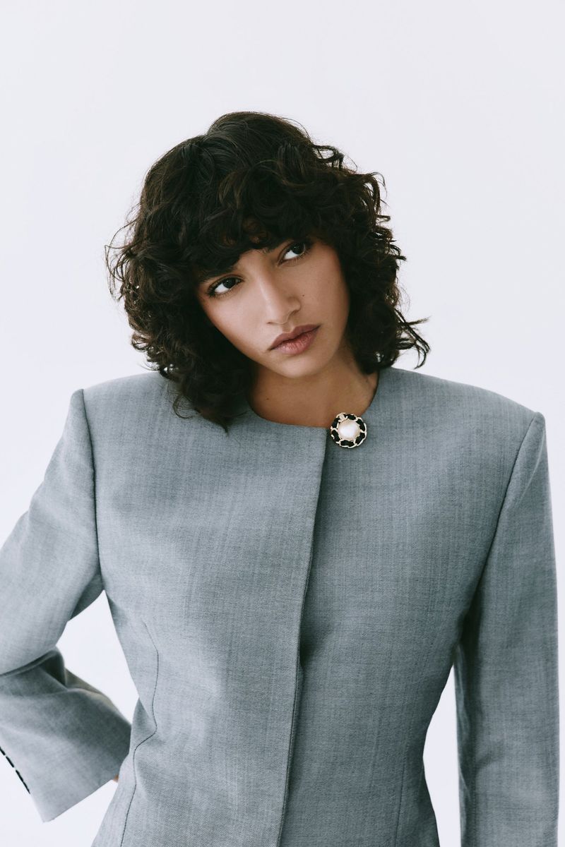 Portrait of a woman in a grey blazer looking to the side against a white background, fashion editorial style, studio lighting, neutral colors.