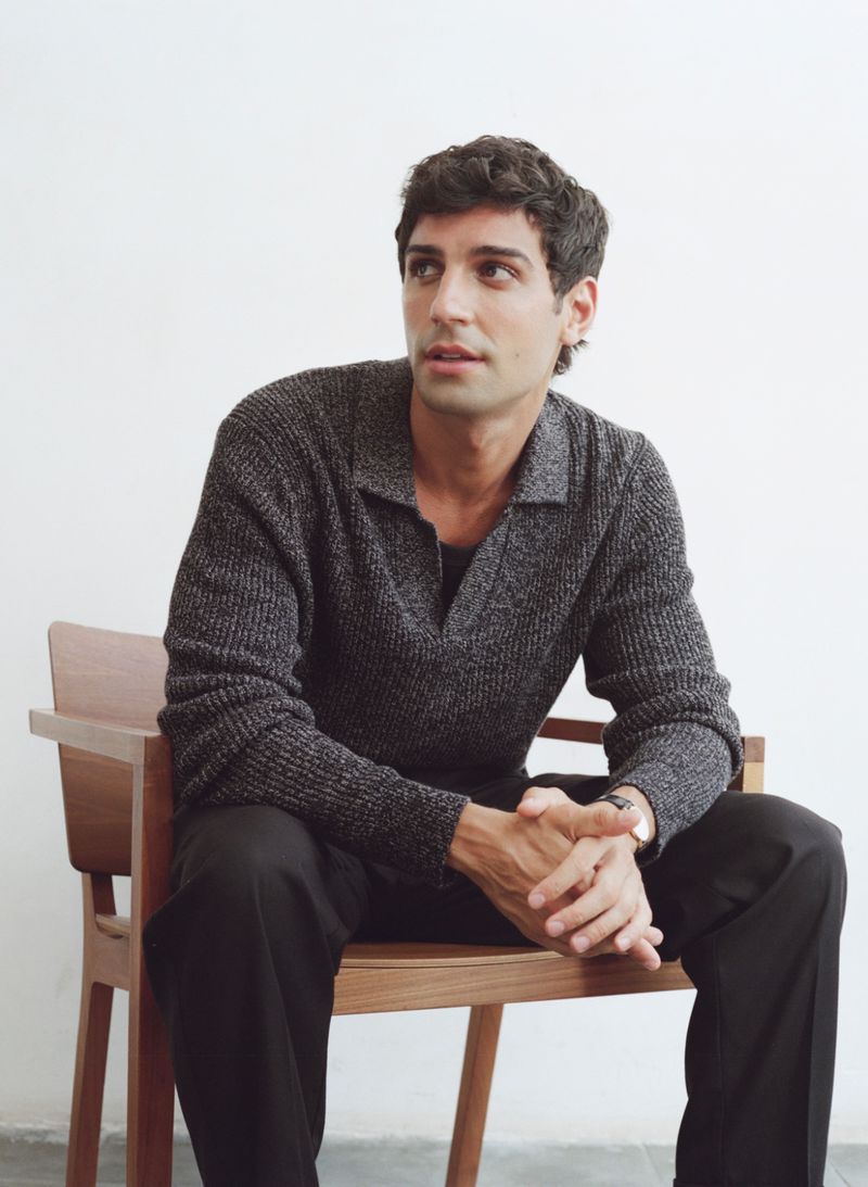 Model Francisco Faria seated in a wooden chair wearing a textured grey polo shirt for Mango Men October 2025.